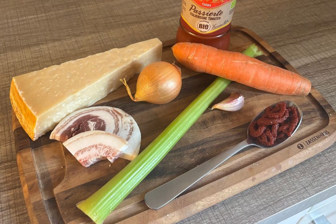 Zutaten für Spaghetti Bolognese – Pancetta, Gemüse, Tomatenmark und Parmesan auf einem Holzbrett